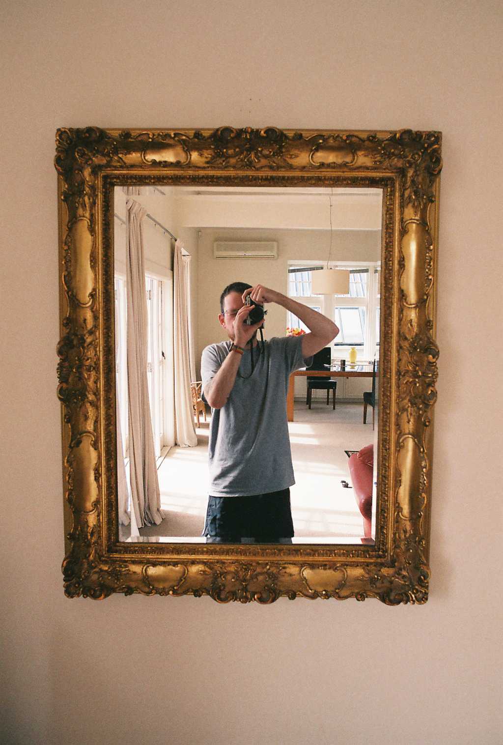A guy holding a camera reflected in a mirror with an ornate frame