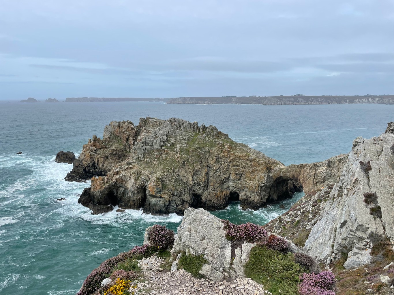 A rocky outcrop surrounded by the sea, connected to the land via a natural narrow rock bridge