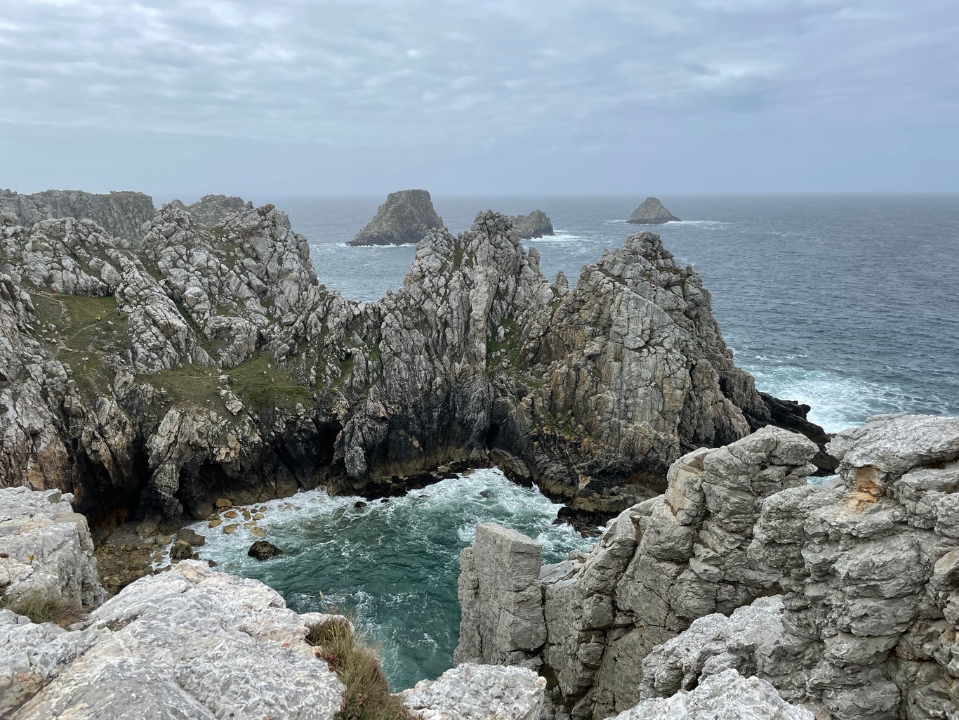 Sharp rocky cliffs giving way to a choppy sea under hazy skies