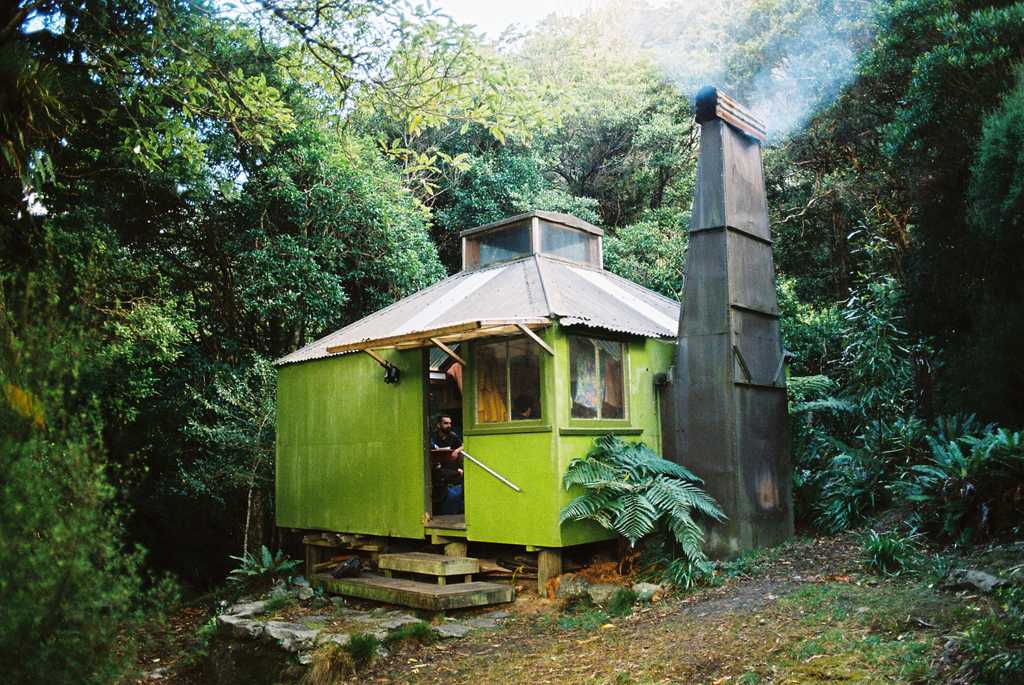 A green hut with the fire lit, situated in native New Zealand bush