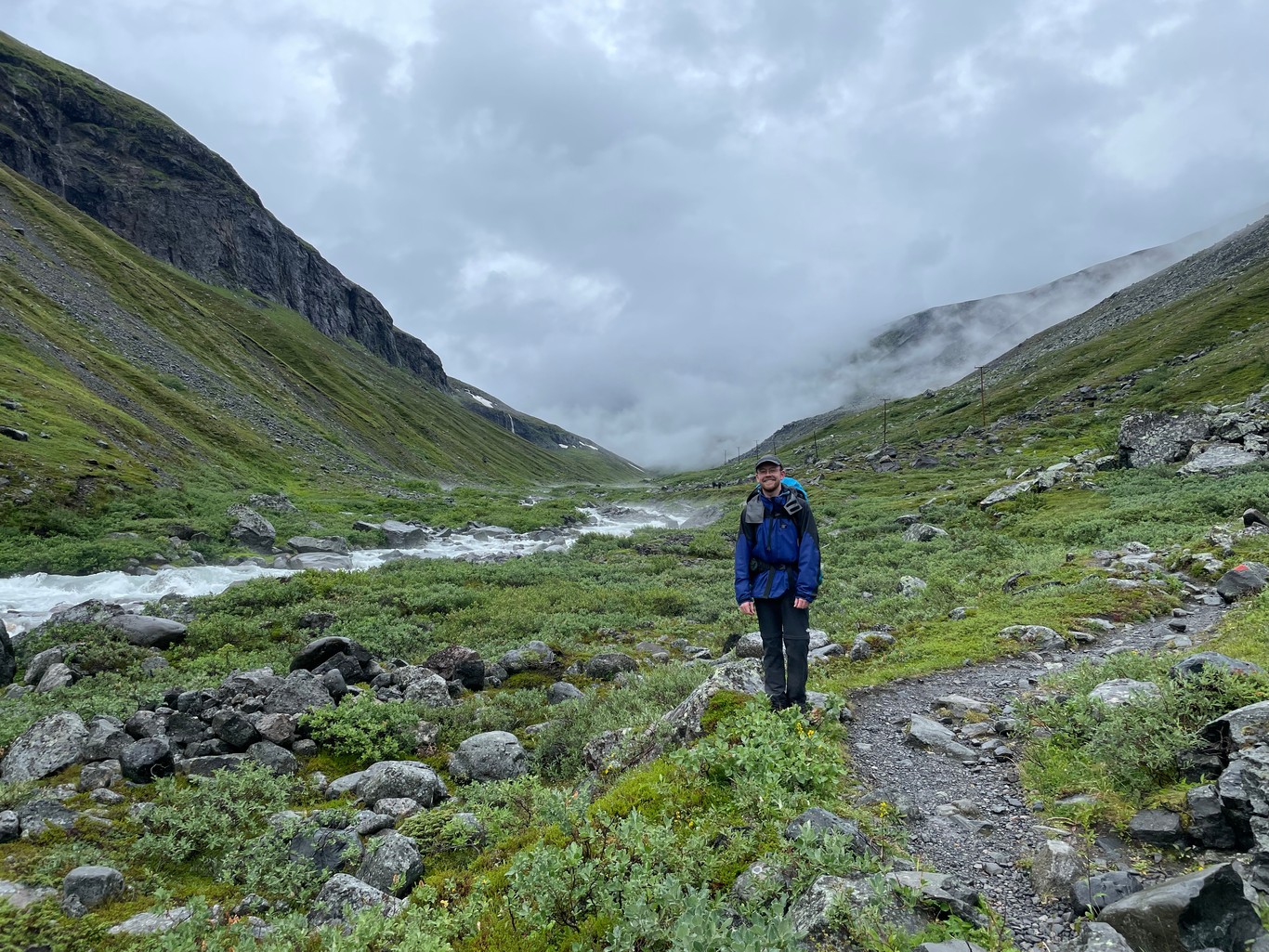 A man standing next to a boulder-filled glacial stream