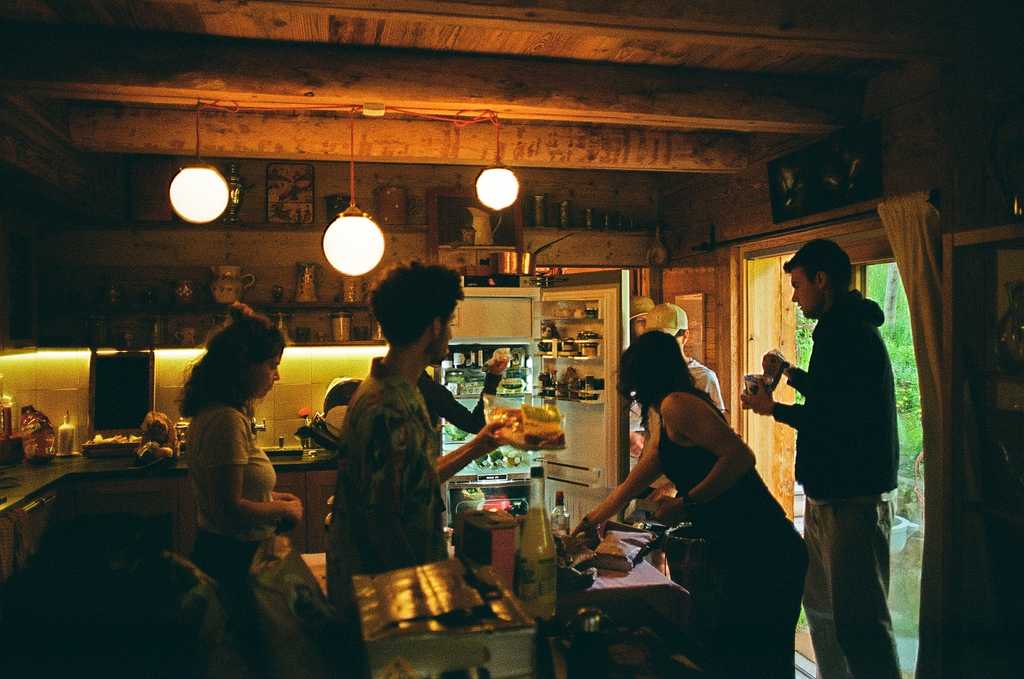 A group of people standing around in a darkened kitchen
