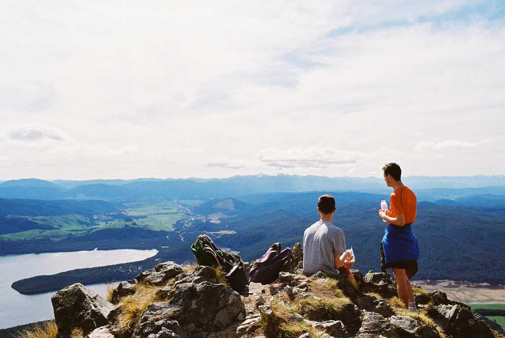Two people sitting on a rocky outcrop overlooking a lake and distant mountains.