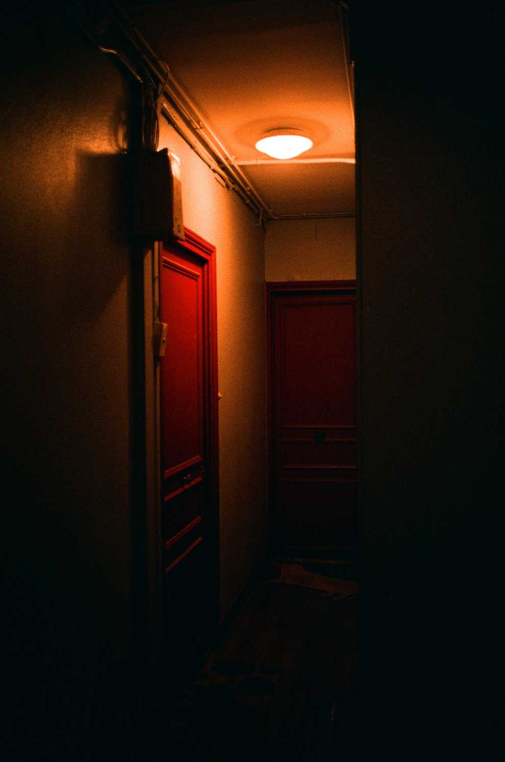 A darkened corridor with a single dome light highlighting two red doors and a box of cables