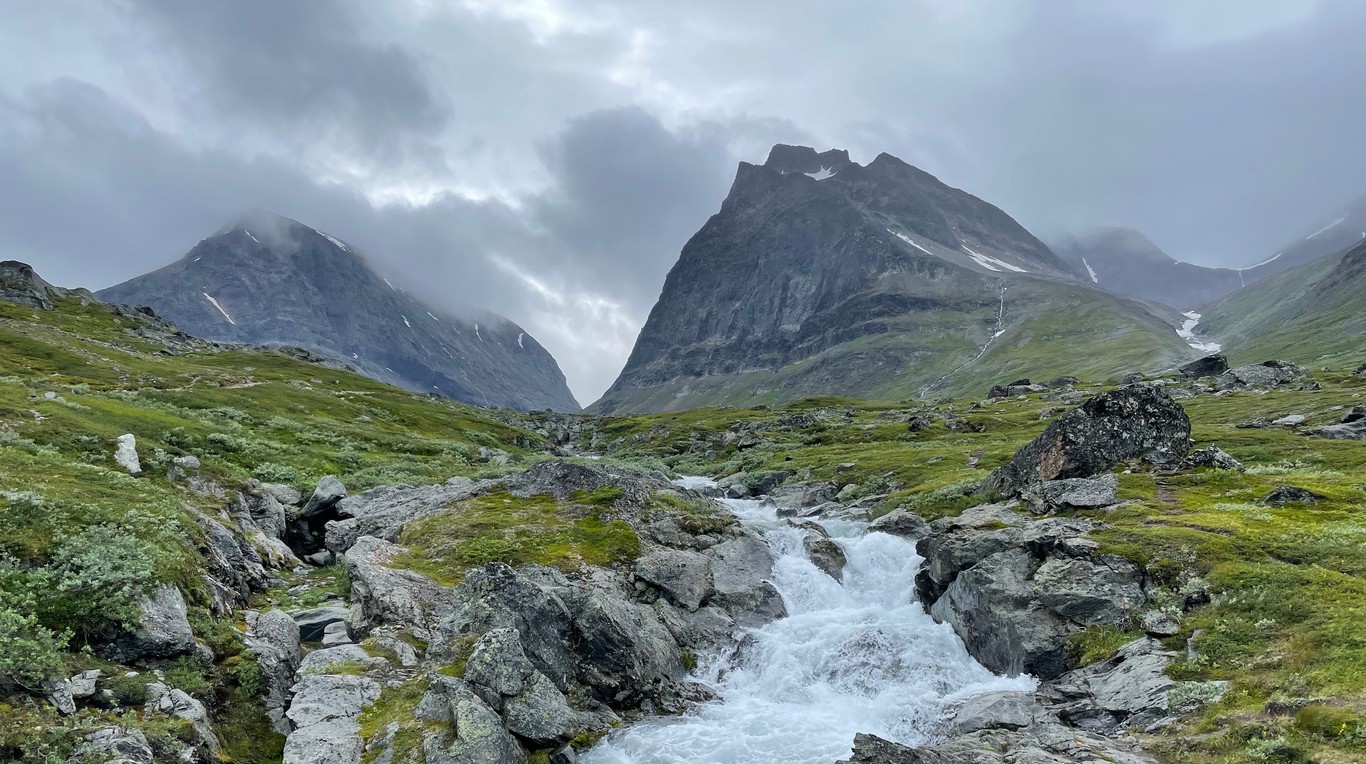 A mountain stream flowing over boulders surrounded by rocky peaks and grey skies