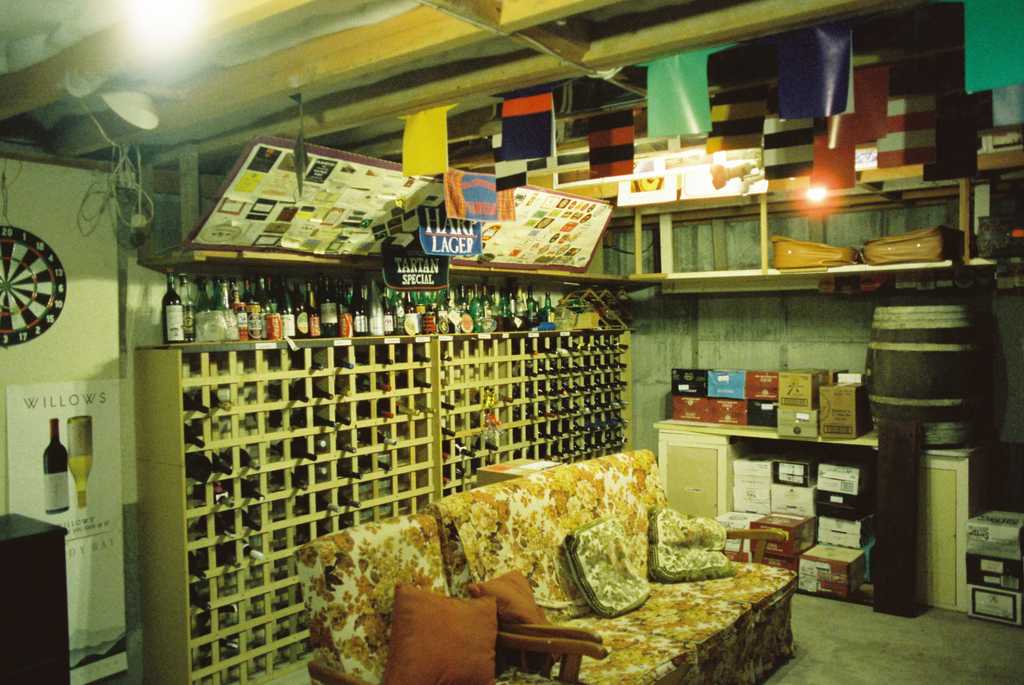 A basement with an old couch, wine rack and rugby shirt posters hanging from the ceiling