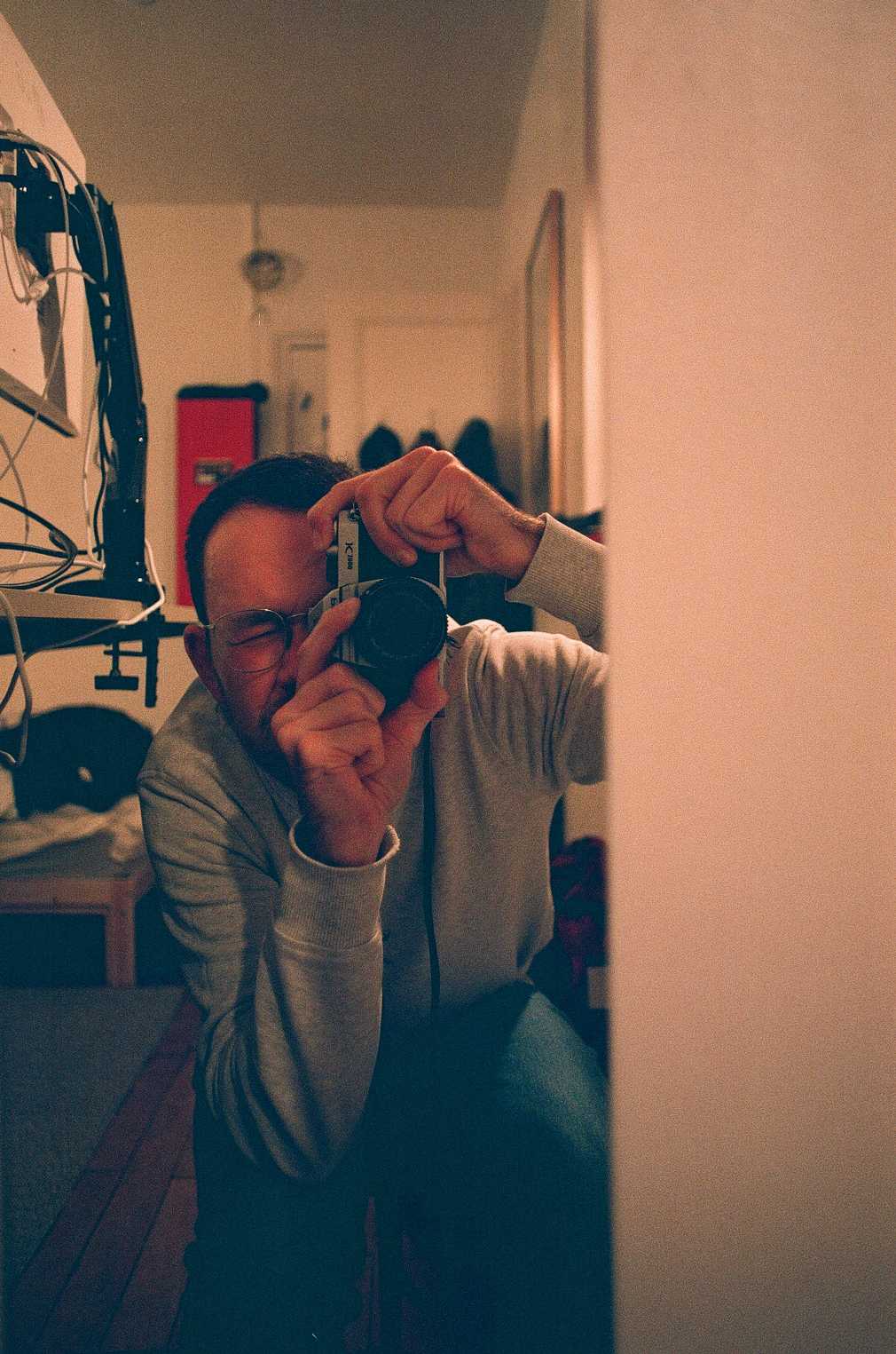 A guy sitting, leaning forward, holding a camera reflected in a long narrow mirror