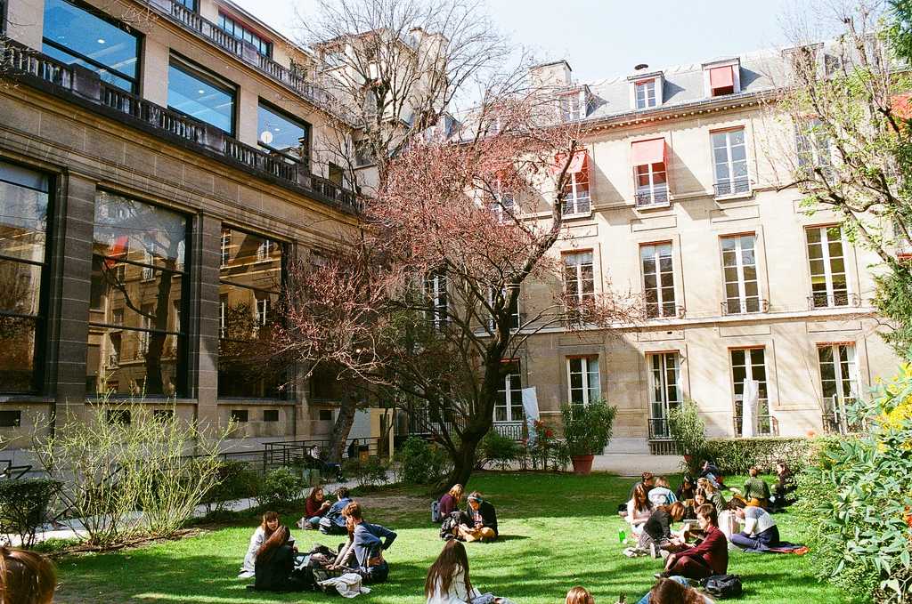 Students sitting on a lawn in a courtyard surrounded by French-style buildings