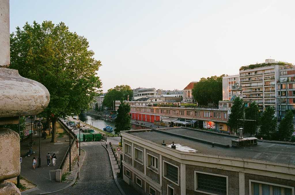 The Canal Saint Martin in the background with the Point Éphémère cultural facility in the background, and a drab concrete building in the foreground