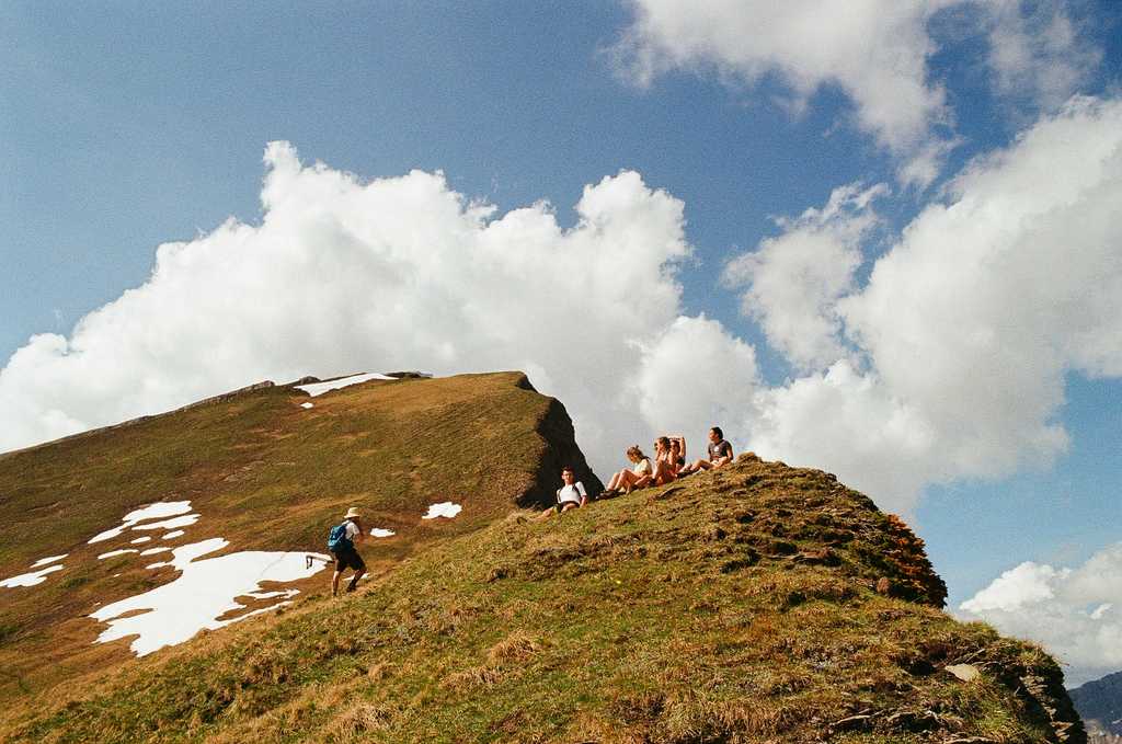 A group of people sitting on a grassy alpine ridge